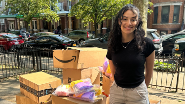 Photo of Angelyse Cardona with boxes of menstrual products to be donated to Asiyah Women's Center