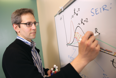 Dr. Nathaniel Hupert writing on a white board.